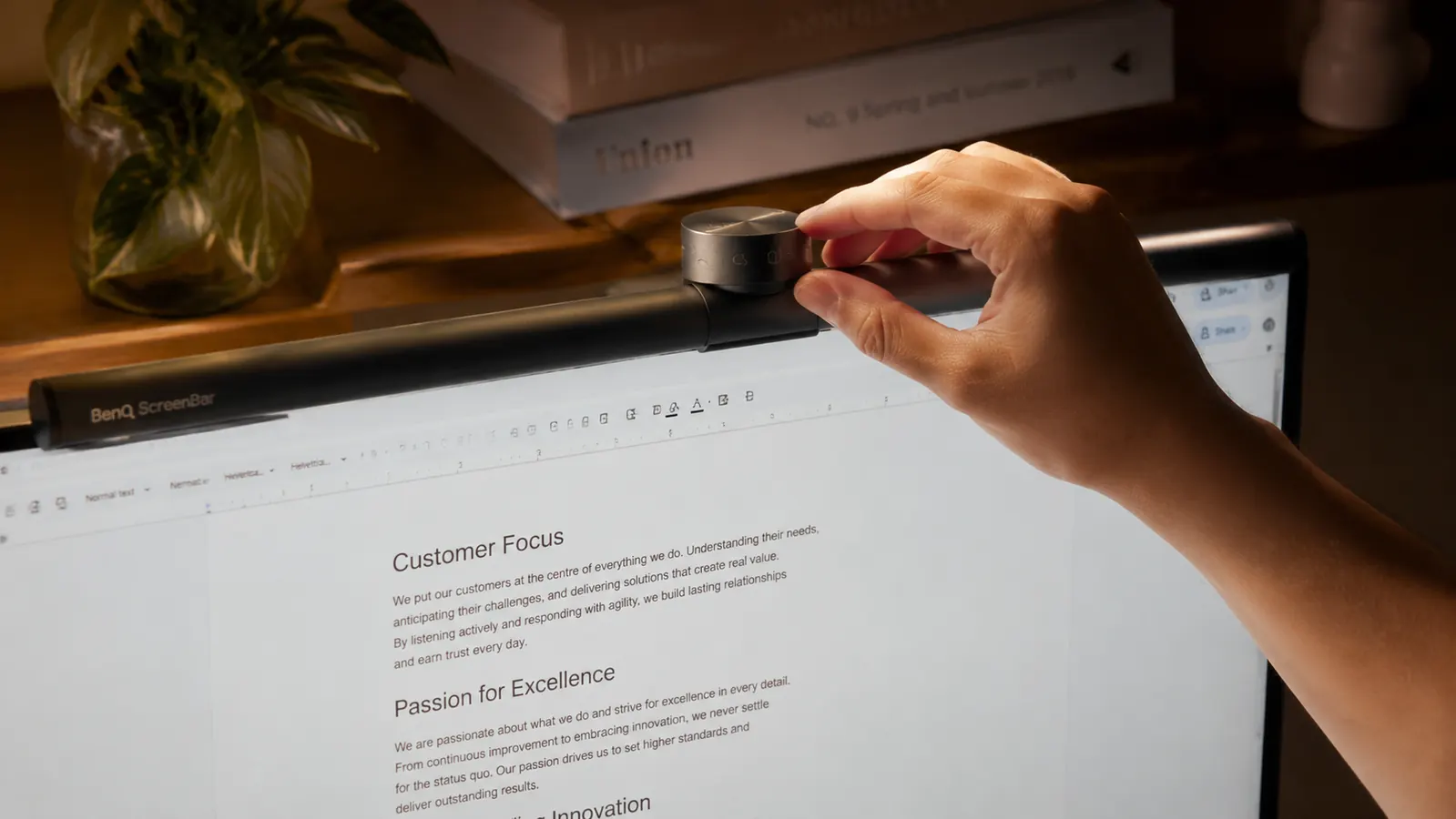 Close-up of a hand adjusting the touch-sensitive dial on a BenQ ScreenBar light bar while the monitor shows a document