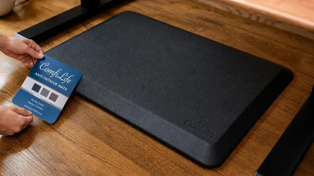 Close-up of black ComfiLife anti-fatigue mat on a hardwood floor under a standing desk